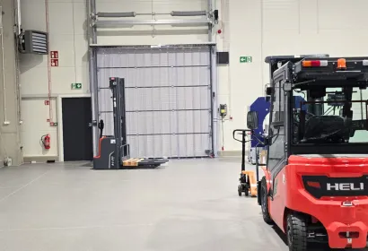 Kurtyna paskowa PCV w wysokiej bramie hali magazynowej, przed nią wózek widłowy i wózek paletowy